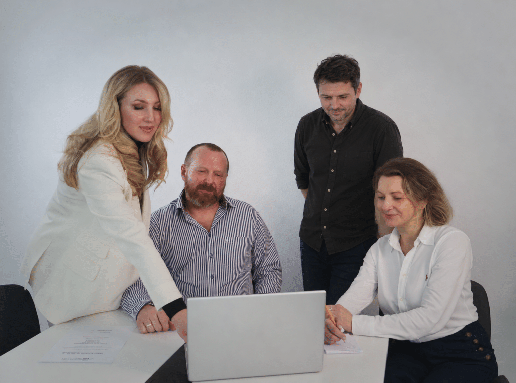 Vier Personen der Kramlich Group bei einer gemeinsamen Besprechung am Laptop. Fotografie teilweise mit KI bearbeitet.